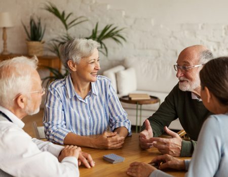 Group of four cheerful senior friends, two men and two women, sitting at table and enjoying talk after playing cards in assisted living home
