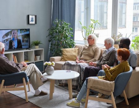Group of senior people resting on sofa in the living room and watching news on TV together